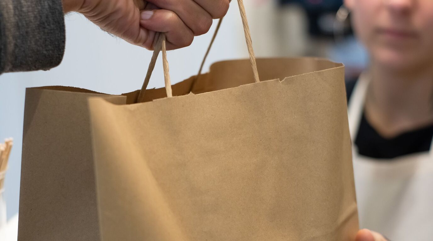 En un mostrador, una mano entrega una bolsa de papel kraft